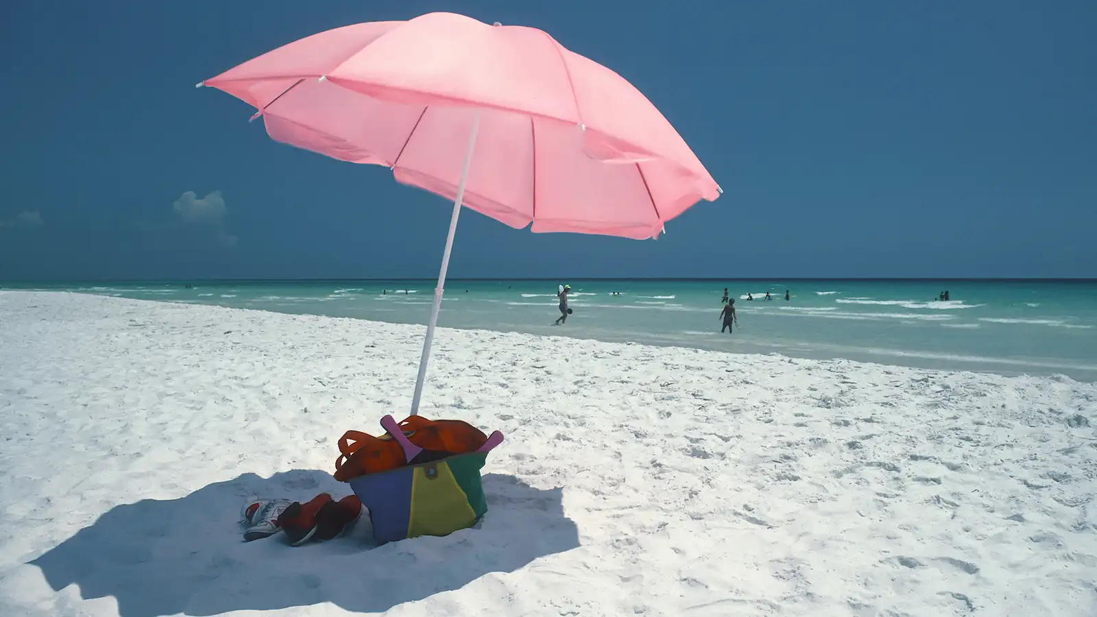 A pink beach umbrella and beach bag on the white sand at Seaside, Florida